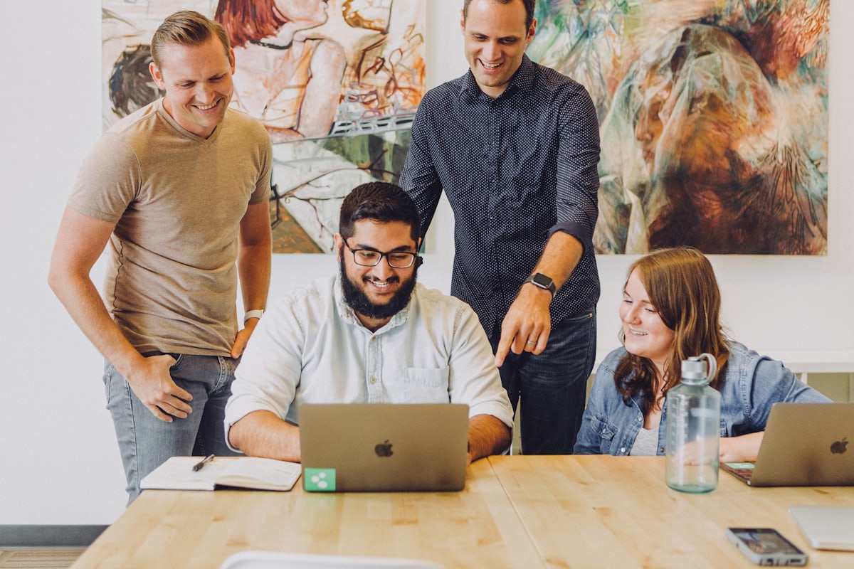 Equipe sorridente colaborando em volta de um notebook durante o desenvolvimento de um projeto